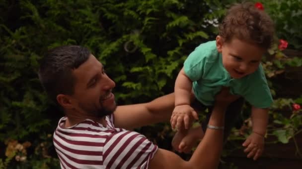 Handsome dad in a striped T-shirt plays and kisses a curly happy baby boy — Stock Video