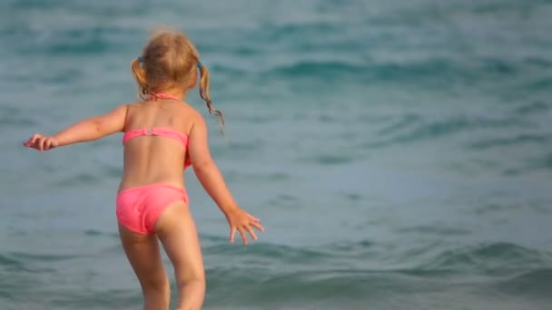 Kleines süßes Mädchen im rosa Badeanzug läuft in der Brandung des Meeres — Stockvideo