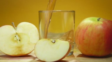Elma suyu, sarı arkaplanda büyük elmaların yanına bir bardağa doldurulur.