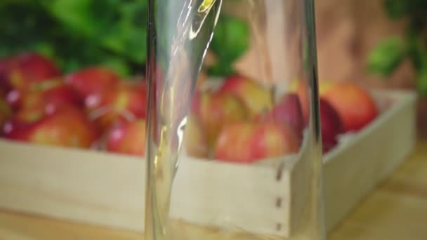 Сок наливают в кувшин рядом с яблоками на фоне зелени — стоковое видео