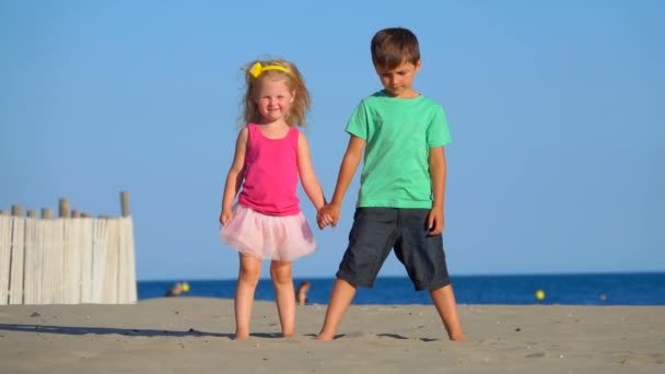 Niño y niña en falda rosa están de pie en la playa y lanzando arena — Vídeo de stock