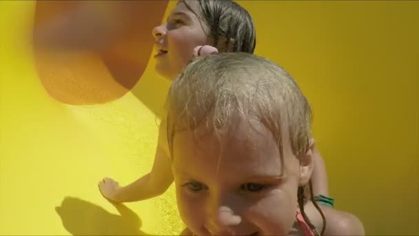 Twee broers en zussen rijden van een sinaasappelglijbaan in een waterpark. — Stockvideo