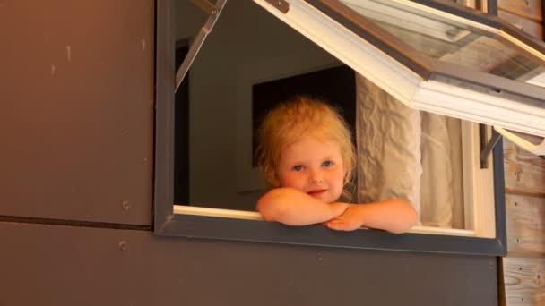 Little sad girl looks out of the open window of the house — Stock Video