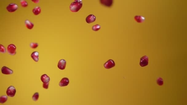 Saftiga korn av granatäpple faller diagonalt på den gula bakgrunden — Stockvideo