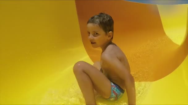 Jongen rijdt over een oranje glijbaan in een waterpark. — Stockvideo