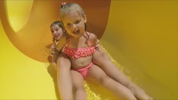 Twee blonde broers en zussen rijden van een sinaasappelglijbaan in een waterpark. — Stockvideo