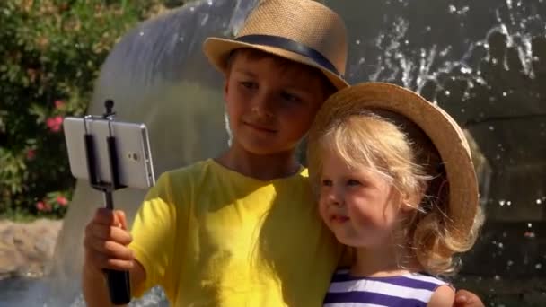 Αγοράκι και κορίτσι με καπέλα βγάζουν σέλφι στο smartphone την ηλιόλουστη μέρα. — Αρχείο Βίντεο