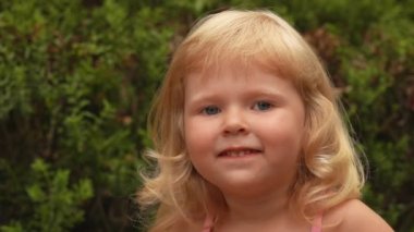 Küçük sarışın bir kızın portresi. Gülümseyen ve elleriyle başını kucaklayan.