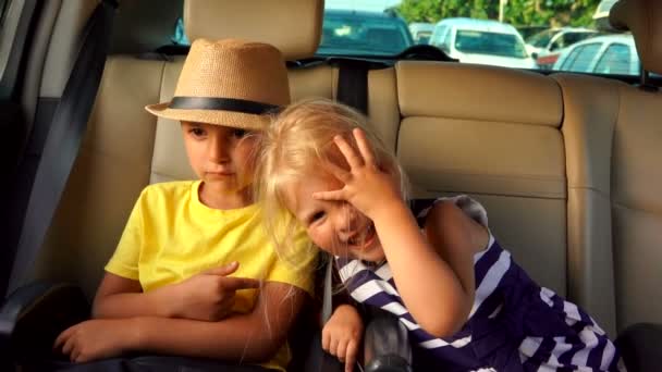 Pequeño niño y niña cabalgando en el asiento trasero del coche y riendo alegremente — Vídeos de Stock