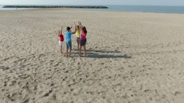 Parlak elbiseli çocuklar kumda zıplar ve ellerini sallarlar.