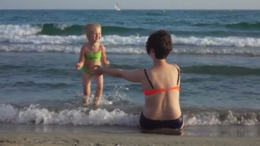 Anne ve kızı sahilde birbirlerine sarılıyorlar.