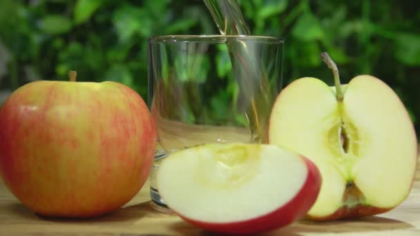 Appelsap wordt gegoten in een glas naast appels op de achtergrond van groen — Stockvideo