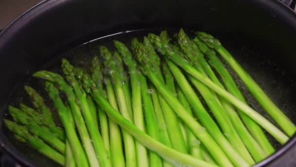 Close-up of peeled green asparagus spears boiling in a black pan — Stock Video