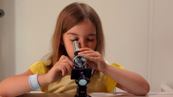 Menina em vestido amarelo está olhando olhar através do microscópio e para a câmera — Vídeo de Stock