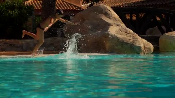 Хлопчик і дівчинка в купальниках стрибають в басейн на відкритому повітрі — стокове відео