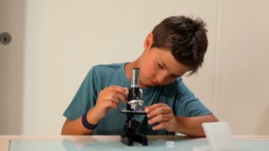 Meraklı siyah saçlı genç çocuk mikroskoptan bakıyor.
