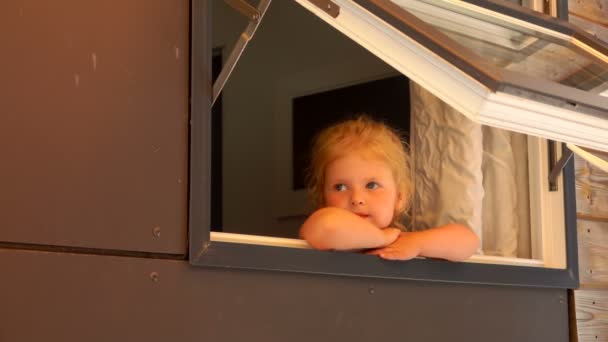 Tankeväckande liten flicka tittar ut genom det öppna fönstret i huset — Stockvideo