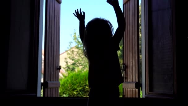 Mała dziewczynka skacze i macha rękami na tle otwartego okna — Wideo stockowe