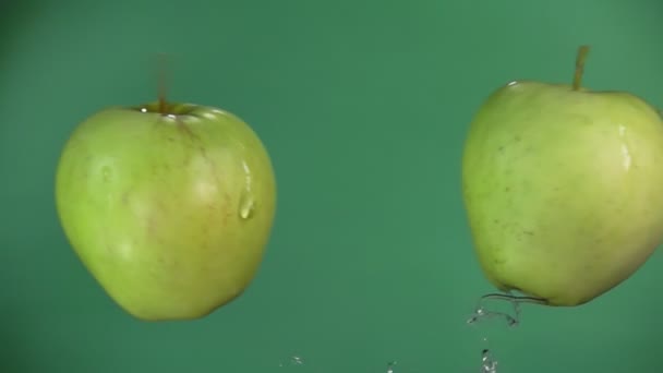 Dvě zelená jablka létají a zpomalují šplouchání vody. — Stock video