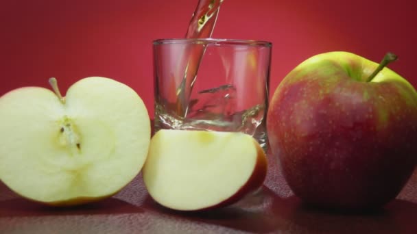 Яблочный сок наливают в стакан рядом с большими спелыми яблоками, разрезанными на ломтики. — стоковое видео