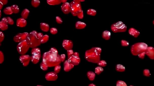 Granos rojos jugosos de granada madura vuelan diagonalmente sobre un fondo negro — Vídeos de Stock