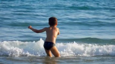 Küçük çocuk su sıçratan bir deniz dalgasında zıplıyor ve dönüyor.