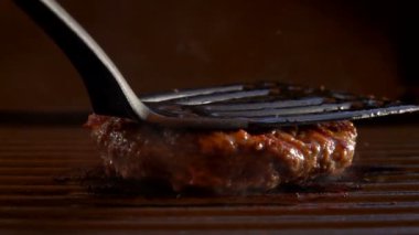 Hamburger için sulu sığır pirzolası ızgaraya bastırılır ve alev alır.