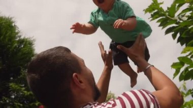 Çizgili tişörtlü yakışıklı baba kıvırcık bir erkek bebek fırlatıyor.
