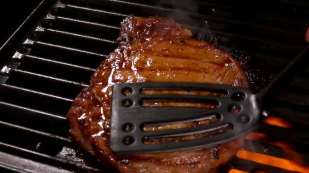 Koch drückt das leckere Steak mit einem Spachtel auf die heiße Oberfläche des Grills — Stockvideo