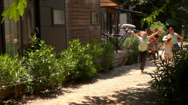 Vrolijke groep kinderen rennen langs de witte weg tussen de huizen — Stockvideo