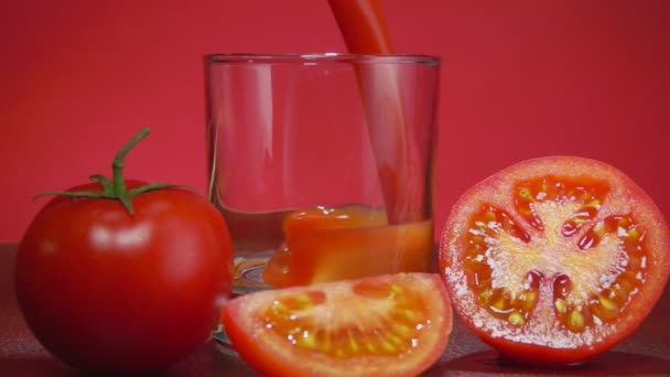 Tomatensaft wird in ein Glas neben reife Tomaten auf rotem Hintergrund gegossen — Stockvideo