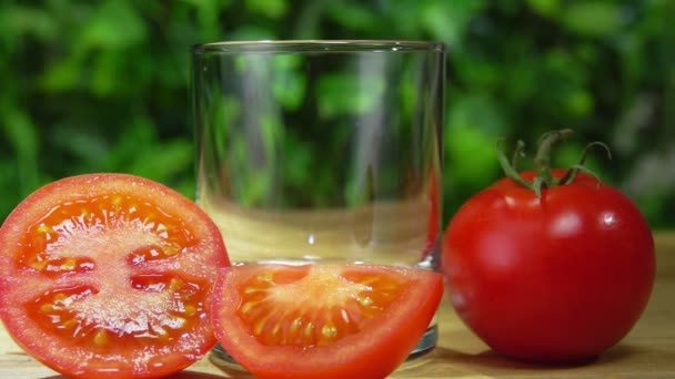 Sumo de tomate flui em um copo ao lado de tomate maduro no fundo da vegetação — Vídeo de Stock