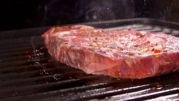 Ein rohes, dickes Fleischsteak brutzelt auf der heißen Oberfläche des Grills — Stockvideo