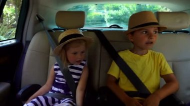 Güzel bir oğlan ve şapkalı sarışın bir kız arabanın arka koltuğundalar.