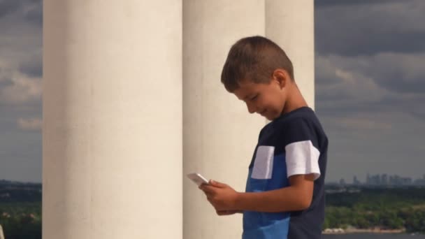 Серьезный загорелый мальчик смотрит на телефон в своих руках — стоковое видео