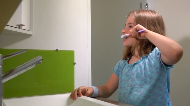 Chica alegre en la blusa azul se cepilla los dientes en el baño — Vídeos de Stock