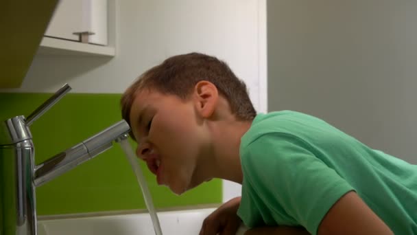 Kleine vrolijke jongen in een groen t-shirt spoelt zijn mond na het tandenpoetsen — Stockvideo