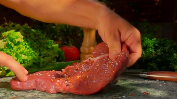 Ruka obrací syrový steak na kamenný stůl, aby ho posypala kořením. — Stock video