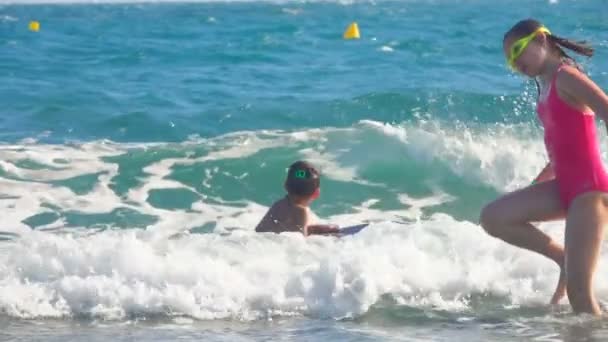 Niño y una chica en un traje de baño rosa están saltando en la línea del mar surf — Vídeos de Stock