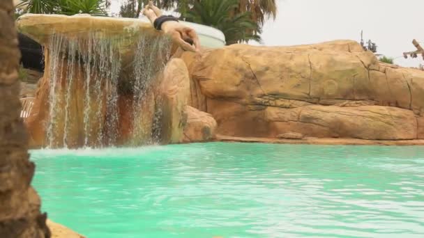 Hombre joven se sumerge en la piscina en el fondo de una cascada — Vídeo de stock