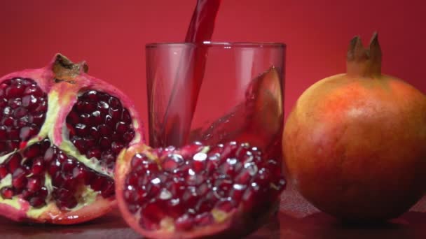 Pomegranate juice is flowing into a small glass next to the ripe pomegranates — Stock Video