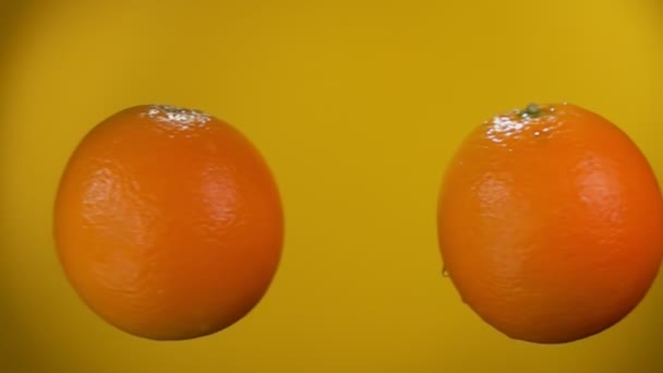 Dos naranjas están volando y chocando entre sí en el fondo amarillo — Vídeos de Stock