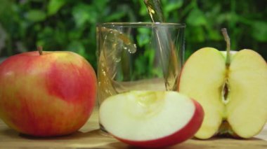 Yeşilliğin arka planındaki bir bardağa lezzetli elma suyu dökülüyor.
