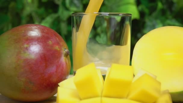 Mango juice hälls i ett glas bredvid stor mogen mango skuren i skivor — Stockvideo