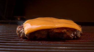 Lezzetli çizburger pirzolası ızgarada kızarıyor, üstünde peynir var.