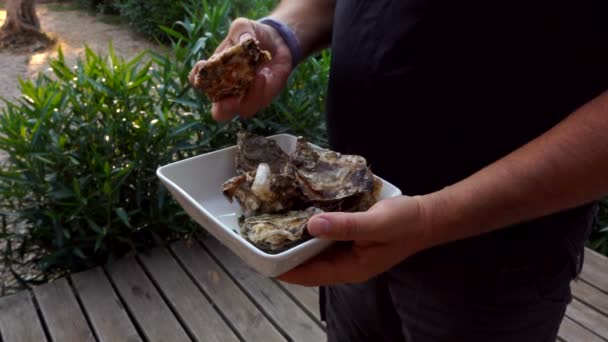 El hombre está sosteniendo un plato cuadrado blanco con ostra fresca deliciosa y recogiendo uno — Vídeo de stock