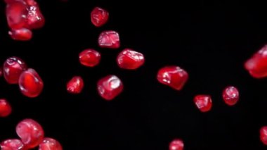 Sulu kırmızı nar taneleri siyah bir zemin üzerinde dönüyor.