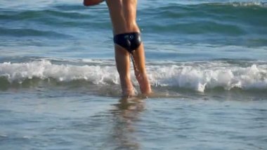 Neşeli küçük çocuk deniz dalgalarına atlıyor.