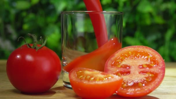 Tomatjuice hälls i ett glas bredvid tomat på bakgrunden av grönska — Stockvideo