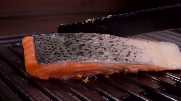 Cocinar voltea un trozo de filete de salmón con espátula negra en la parrilla — Vídeo de stock